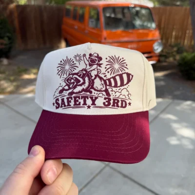 Natural and maroon hat with Safety 3rd lettering and a cowboy pug riding a raccoon, front view.