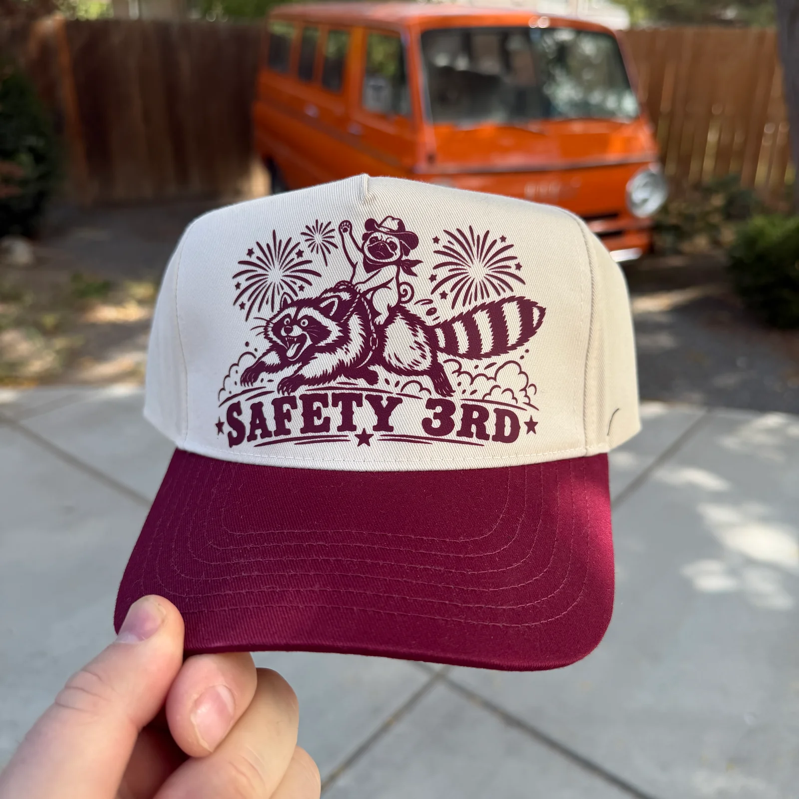 Natural and maroon hat with Safety 3rd lettering and a cowboy pug riding a raccoon, front view.