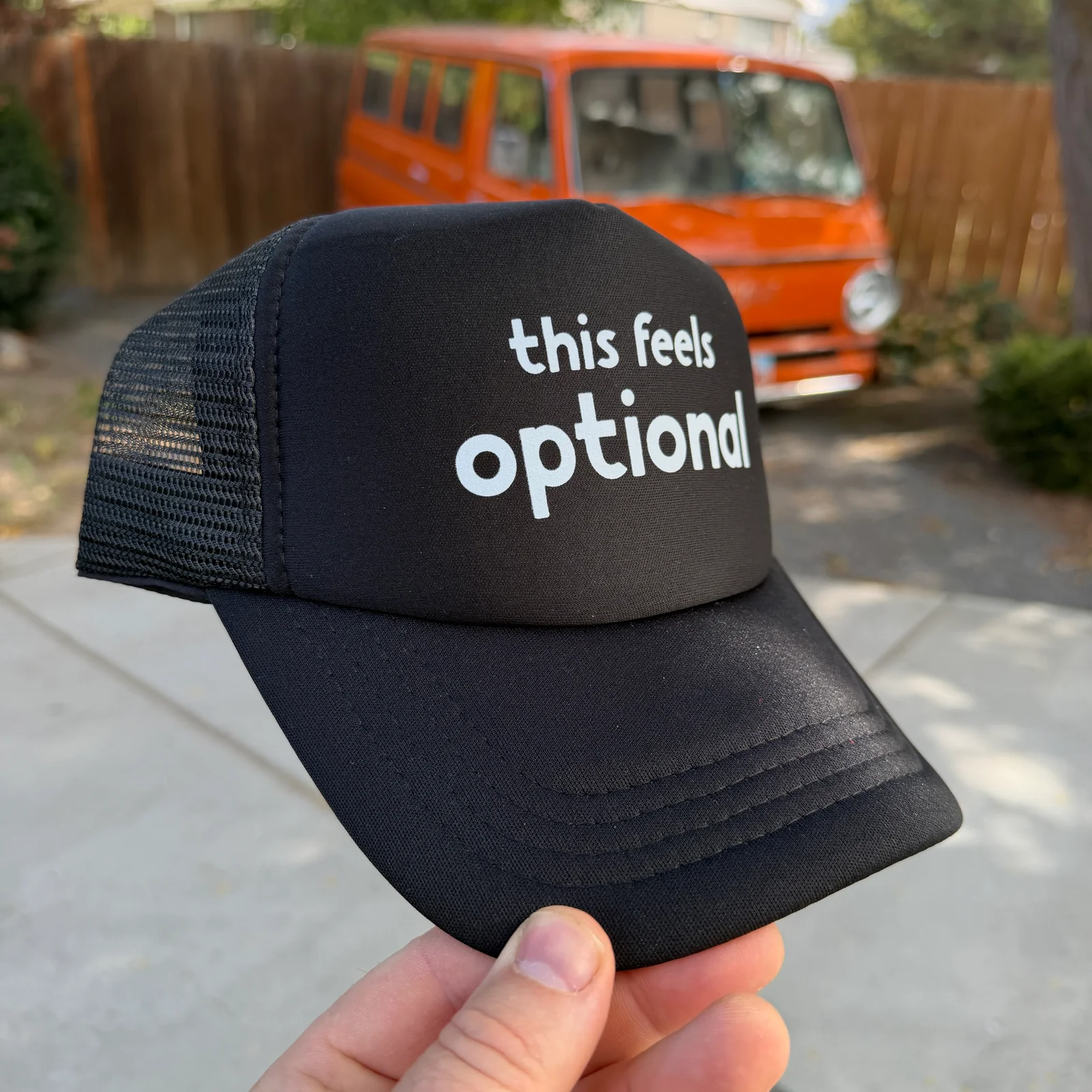 Black foam-front mesh trucker hat with white This Feels Optional lettering, front view.