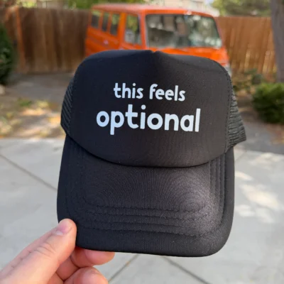 Black This Feels Optional trucker hat showing the printed front and mesh side.